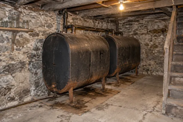 Two old black heating oil tanks joined by pipes in a fieldstone cellar